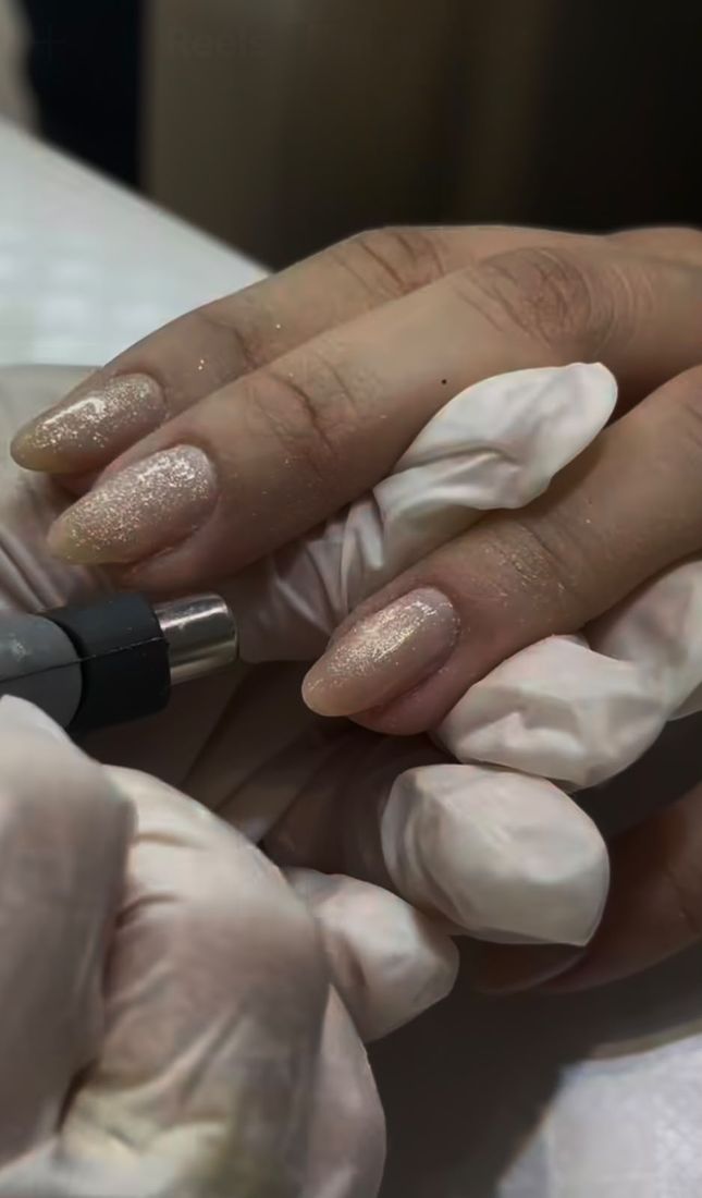 Profissional do A Louise finalizando unhas com glitter dourado, usando luvas